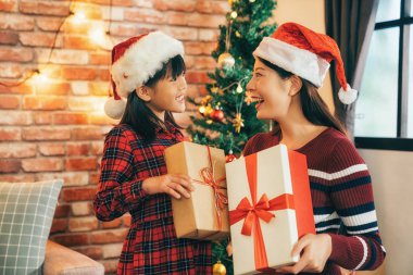 oturma odasında sevimli kız için hediye göndermek zarif anne. iki kız Noel arifesinde Noel Baba şapkası giyiyor. Noel ev concept kutlamak. boks gününde hediye online alışveriş.