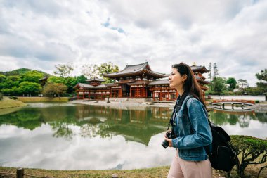 Tapınağın arka planda havuzun etrafında yürüme zarif kadın gezgin. Kyoto tatile turist kadın seyahat. Byodo yılında güneşli bir günde yeşil havuzun yer alan.