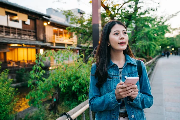 現代の女性は 彼女の携帯電話を保持し 夕日を見て道路に立っています 少女都市旅行京都先ランドマーク有名な観光地で観光 旅行者が携帯電話で方向性を見つける — ストック写真