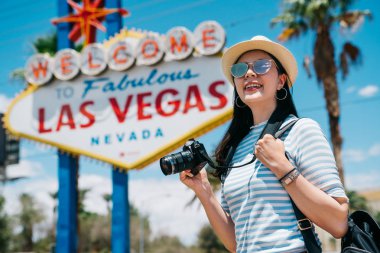 sevinçle kamera ayakta Las Vegas sokakta güneşli günde taşıyan kadın fotoğrafçı. Bayan objektif adam slr kamera ayakta las vegas altında imzalamak Tur gezi Amerika'da tutarak yola.