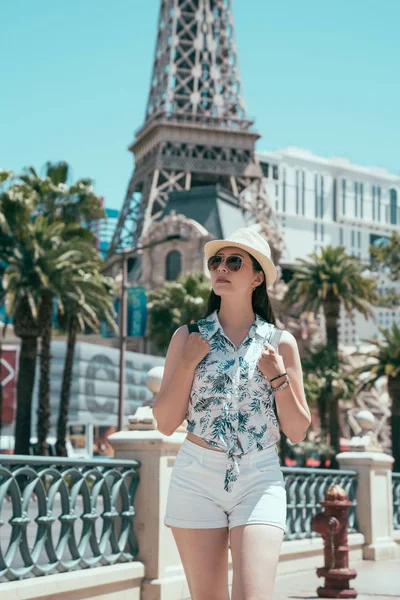 Genç backpacker yanındaki uzun boylu kule yürüme. güzel Bayan turist şapka ve güneş gözlüğü ile las Vegas'ta yaz aylarında seyahat. Vegas tatil sahip kadın gezgin.