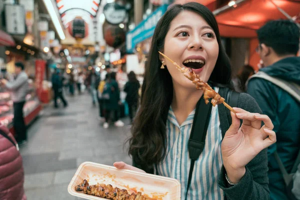 快乐的女人体验当地的日本文化吃美味的烤鸡肉串 在日本的室内市场上吃东西的游客们很快乐 在大阪的市场 — 图库照片