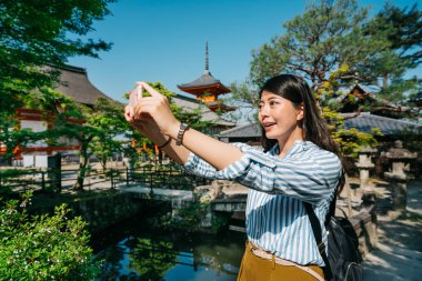kadın turist alarak resmi Japonca tapınak Bahçe en güzel manzara. telefon ile yeşil pond, selfie alarak genç yolcusu. Güneşli bir gün içinde belgili tanımlık geçmiş Budist pagoda ayakta.