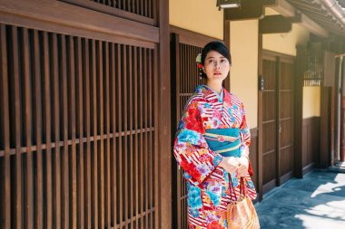 Japon kız arkadaşı için bekleyen onun evinin önünde renkli kimono ayakta giyiyor. ahşap Japon evin yanındaki çiçek kimono ile genç bayan. Japon yerel halkın yaşam tarzı.