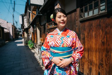Eski şehrin yüz çekici bir gülümseme ile kırmızı kimono ayakta Japon kızla. bayanın çiçek kimono tarihsel caddenin Kyoto'da güneşli günde yürüyüş.