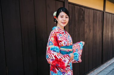 kimono konumu Japonya ve kamera gülen yüze eski şehirde olan genç yolcusu. Kyoto arka planda ahşap duvar ile kız turist çiçek kimono kılığına girmiş. Kyoto seyahat tatil keyfini çıkarın.