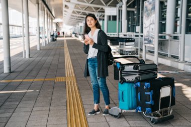 Asya işkadını kansai Uluslararası Havaalanı ve otobüs tarifesi online cellphone tarafından arama açık duran arrive. Bagaj taşıma için bekleyen genç kadın. iş yurtdışında yaşam.