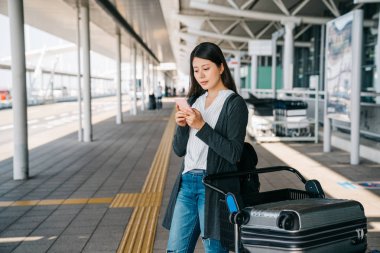 Genç Asyalı yolcu Bagaj arabası duran ve cep telefonu kullanarak. zarif kız turist gelmesi osaka Havaalanı ve şehir gezi Başlat. Tur Rehberi mesaj App online için başvurun.