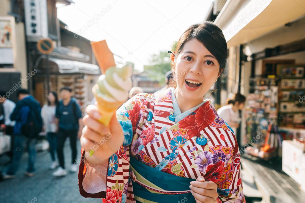 tourist experience Japanese culture, wearing kimono and trying the famous matcha ice cream in Kyoto. young girl traveler in japan tours. asian face to camera showing sweet.