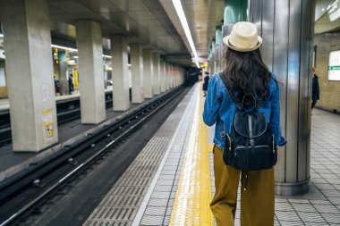 arkadan görünüşü kadın backpacker Japonya'nın osaka Metro İstasyonu platformunda yürüme. uzun siyah saçları giyen ile Genç Asyalı kız hasır şapka. yoğun kentsel underground taşımacılığında.