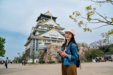 Giriş ücreti arama telefon kullanarak osaka Kalesi önünde duran çekici gezgin. güneşli günde gülümseyen genç kadın turist neşeli yüz fotoğraf makinesi. güzel Bayan tatil yaşam tarzı.