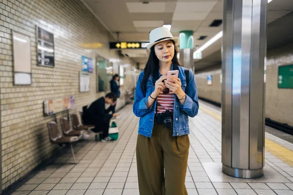 地下鉄のスケジュールをチェックする携帯電話アプリケーションを使用して若い旅行女性 帽子地下駅を歩いて女性の観光客 携帯で観光スポットを検索女の子バックパッカー — ストック写真
