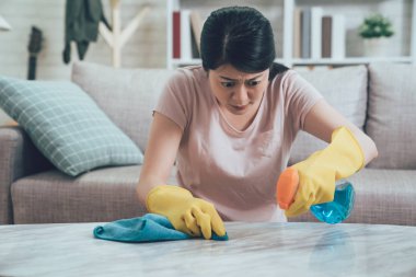 papatyanın genç bayan püskürtme temiz temizlemek için bez kullanarak eldiven giymiş mermer masanın üzerine yoğunlaştı. odak kadın evde gündüz temizlemenizi t gömlek. arka planda rahat kanepe