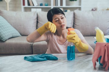 Asyalı kadın onun ev ev işleri yaparak güzel ve yorgun hissediyorum. koruyucu giyen genç ev hanımı silme ter bütün gün evde ev işi yaparken dinlenme eldiven. Tablo kovanın içinde temizlik malzemeleri.