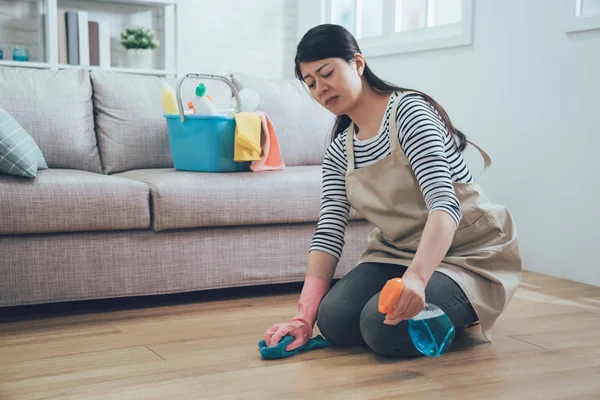 洗浄剤を見て若いアジア女性折り敷きリビング ルームの床を強調しました 顔をしかめ主婦怖がって自宅家事スプレー洗剤を使用しています 不幸な家政婦を雑巾で拭く — ストック写真