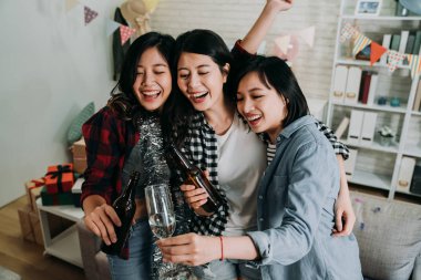 ev partisi kızlar sevinçle birlikte şampanya bardağı kızartma sarılma. kaygısız arkadaşlar eller yükselterek hediye kutuları yerdeki ile evde partinin tadını çıkar. bira ve şarap alkış tutan Asya bayanlar.
