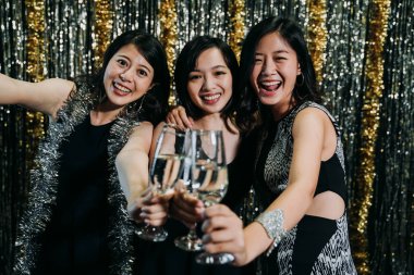 Şarap bardakları toasting neşeli kız kameraya karşı karşıya. Şampanya büyük diş gülümseme ile tıklayarak genç arkadaşlarım. xmas kutluyor kulübünde eğleniyor parti elbiseler giyen güzel bayanlar