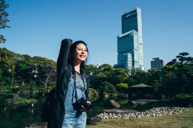 neşeli gezgin güneşli gün hareketleri saç üzerinde açık duran kamera taşıyordu. sevinçle güneş zevk gülümseyen genç kadın fotoğrafçı. arka planda Japonya'nın osaka Abeno harukas.
