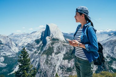 yosemite Milli Parkı ve yarım kubbe göz dağı tepesinde yer kontrol cep telefonu bulma tutan kadın gezgin. şaşırtıcı doğa manzaralı güzel mavi gökyüzü.