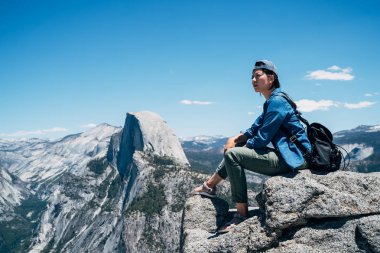 Gezgin yosemite Milli Parkı içinde dağın tepesinde oturan şapkalı. Genç Asyalı backpacker seviyorum ABD'de yaz seyahat hiking. güzel mavi gökyüzü şaşırtıcı doğa ile yarım kubbe görüntülemek