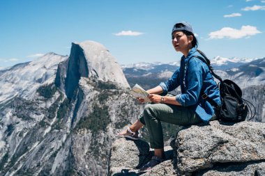 cool kadın backpacker yosemite Milli Parkı içinde dağın zirvesinde büyük kayanın üzerine oturmuş. Genç Asyalı hiker seyahat hiking içinde hedef kontrol kağıt harita tutarak. kadın backpacker zevk görünümü