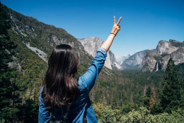 arkadan zafer parmak işaretiyle eller yükselterek genç kadın backpacker görünüşü. kaygısız kadın uzun yürüyüşe çıkan kimse doğa dağ yosemite Milli Parkı Kaliforniya Amerika'nın tadını çıkarın. güzel manzara mavi gökyüzü altında