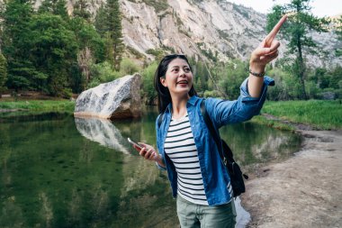 neşeli uzun yürüyüşe çıkan kimse kadın gökyüzüne gezi ayna göl yaz yürüyüş gezisi sırasında işaret heyecanlı. Internet üzerinde Yosemite konaklama bulma holding cep telefonu gülümseyen genç kız gezgin.