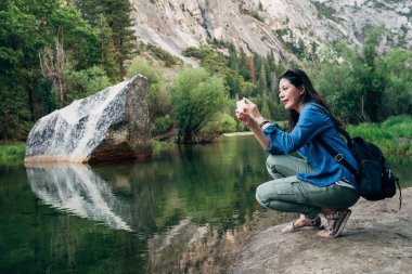 Asya seyahat kadın cep telefonu resim şaşırtıcı doğa görünümü ayna göl yosemite Ulusal Parkı içinde bizi çekmek tutarak diz çökmüş. sırt çantası aşk vahşi seyahat gezi ormandaki ile genç kız uzun yürüyüşe çıkan kimse.