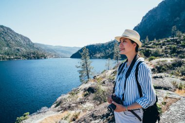 Asyalı kız fotoğrafçı Holding dslr gülümseyen doğa görünümü hetch hetchy baraj gölünün gezi fotoğraf makinesi. Genç Bayan turist yosemite Milli Parkı seyahat gezi san franisco'içinde güneşli günde hiking.