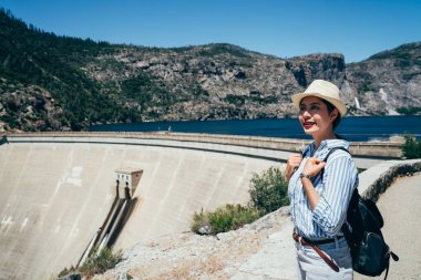 Genç kız gezgin Hetch Hetchy rezervuar barajda O'Shaughnessy ziyaret edin. Asyalı kadın gülümseyen güneşli sırt çantası taşıyan şapkalı. sanfranisco yaşam tarzı kavramında seyahat.