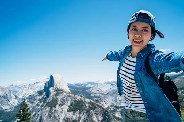 happy girl hiker taking selfie on the top of mountain in yosemite national park travel. young carefree asian backpacker showing the beautiful natural view with blue clean sky on sunny day lifestyle.