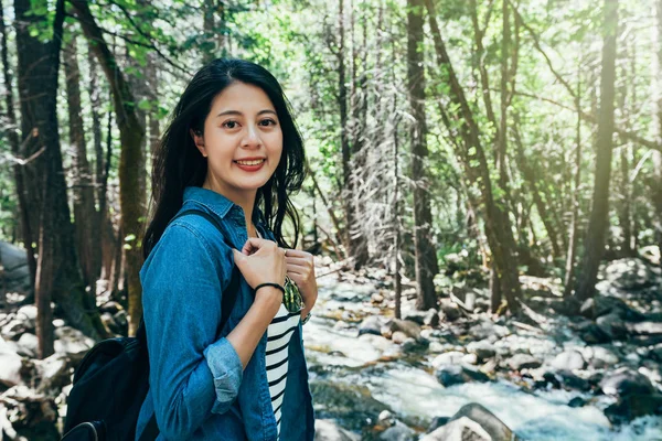 female backpacker face camera giving confident smile. young lady hiker love wild lifestyle travel hiking trip in forest in yosemite national park in summer. girl standing near the cool lake river.