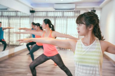 Grup yetişkin spor salonunda kapalı bir yoga sınıfına katılıyor. sportif gençler bir savaşçı yaparken sınıf bir sağlık kulübü, aynaya bakacak şekilde poz. pratik arkadaş birlikte kaygısız açılış silah poz.