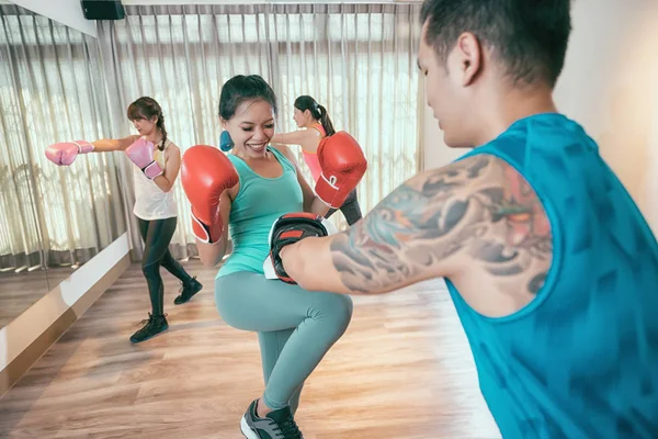 女子踢拳击手踢她的教练在争吵的会议 在背景下 其他拳击手正在练习在空中打拳姿势 一群亚洲女孩在健身房与教练一起上拳击课 — 图库照片
