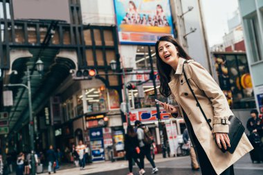 Asyalı kadın cep telefonu online harita yoğun bir gün içinde kentsel yönde arama kullanarak Japonya'da iş seyahat gezisinde. Akıllı holding neşeli genç hanım telefon otel bulma etrafında arıyorum