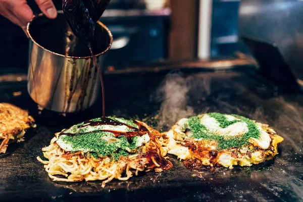铁板烧锅上的奥科诺米烧 厨师把咸味酱汁倒在日本风格的煎饼上 让它吃得很好吃 铁板上的热传统街头食品 — 图库照片