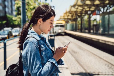 Açık Tren İstasyonu'na metro san Francisco platformda gelmesi için bekleyen işten sonra kadın gidip. kadın gençlerin cep telefonu mesaj yanıtlama e-posta kullanarak toplu taşıma platformu.
