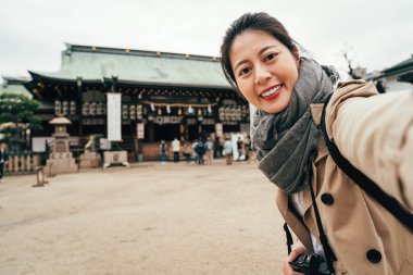 Genç kız tenmangu Tapınağı yüz kamera gülümseyen toprağa ayakta. Selfie tarihi ile çekici Bayan fotoğrafçı osaka Japonya Japonca türbe. Şinto ile kendi kendine portre çekici kadın toursit
