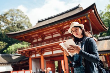 Asyalı Çinli kadın turist rehberi ile büyük tapınak yaptırın. Genç kız Kasuga taisha geçmiş bilgilerini gezi nara Japonya ziyaret ederken güneşli okuma. geleneksel eski mimari.