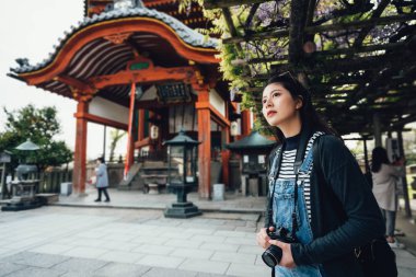 Genç kız turist fotoğrafçı alarak fotoğraf gezi kofukuji nara Japonya ziyaret ederken slr fotoğraf makinesi. güzel mor çiçek açan çiçek bahar güneş altında ağaçlar ahşap çatılı.