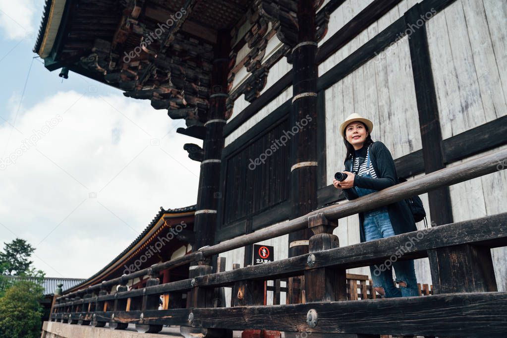 asian tourist woman making pictures in ancient japanese temple. elegant travel photographer with favorite professional camera in todaiji nara japan. girl sightseeing outdoor place of interest.