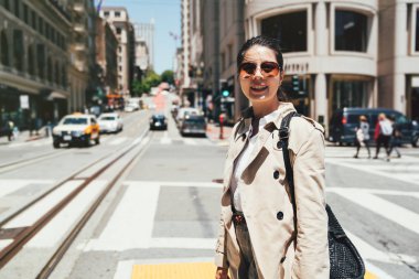 neşeli genç üniversite öğrencisi güneşli günde Zebra kapısı üzerinde yürüme yüz kamera gülümseyen güneş gözlüğü takıyor. İnsanlar san Francisco'da çalışmak için özel araba kullanıyorsun. şehirde taksi taşımaları.