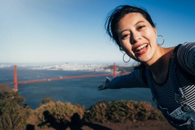 San Francisco Golden Köprüsü seyahat selfie kız. Asyalı kadın yetişkin alarak resim ile ünlü Amerikan cazibe Kaliforniya ABD gösterilen yaz tatil el sırasında onun smartphone.