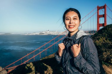 neşeli kadın turist tarafından Golden Gate Köprüsü san francisco gülüyor. güzel kız backpacker dağda duran güneş altında gülümseyen yüz kamera hills. mavi temiz gökyüzü ve deniz okyanus su.