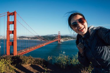 Mutlu genç kadın turist selfie San Francisco Golden Gate Köprüsü ABD tarafından alarak güneş gözlüğü takıyor. Asyalı kadın yüz kamera kendi kendine portre ünlü cazibe ile bizi içeri alarak çekici gülümseyen.