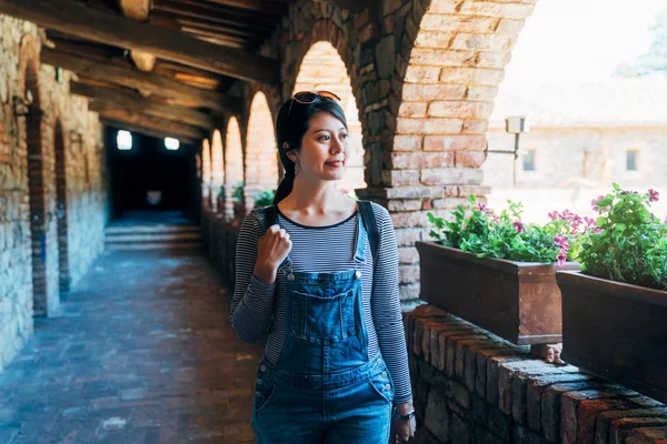 Asyalı kadın ile bitki ve çiçek yanında eski Ortaçağ kale koridor boyunca yürüyüş. Genç kız sevinçle yaz tatil gezisi Avrupa'nın bina tarihinde gezi. kadın güneş gözlüğü.