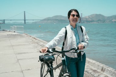 Asya turist kadın kendini Tur gezi san francisco Amerika'da yaz aylarında rehberli sanat eseri aracı olarak bisiklet kullanarak güneş gözlüğü. Genç kız yürümek ile bisiklet ile altın köprü defne Okyanusu yakın.