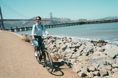 golden gate köprüsü san francisco Kaliforniya ABD gezi gülümseyen kadın binicilik bisiklet seyahat. Genç Bayan güneş gözlüğü plaj deniz okyanus boyunca Bisiklete binme neşeli. Bisiklet üzerinde kadın backpacker.