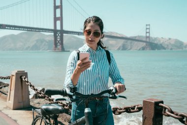 Asyalı kadın kum plaj yaz yaşam tarzı kaygısız boyunca bisiklet ile yürüme. golden gate köprüsü san francisco bisikletle Tur gezi sırasında bilgi arayan cep telefonu kullanan genç kız.