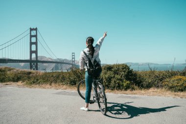 Golden gate köprüsü San Francisco ABD gezi bisikleti kadın backpacker. bisiklet tur zevk ünlü dönüm noktası California üzerinde turist. Kız kaygısız yetiştirme arkadan görünüm el zafer parmak işareti